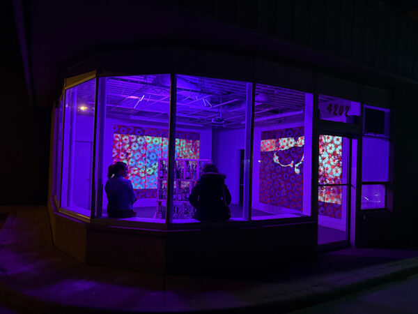 Two people peer into the windows of a gallery at night.