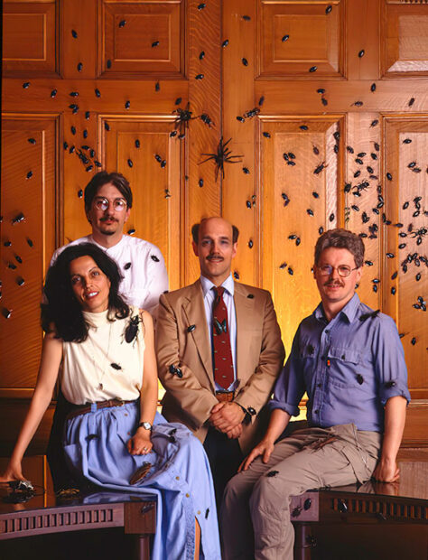 Four people pose for the camera with insects on the wall behind them and on their clothes.