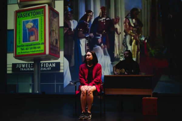 A woman in red sits in front of a large projection of a movie.