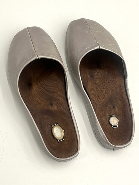 Two leather slippers with a wooden panel inside containing tiny wristwatches.