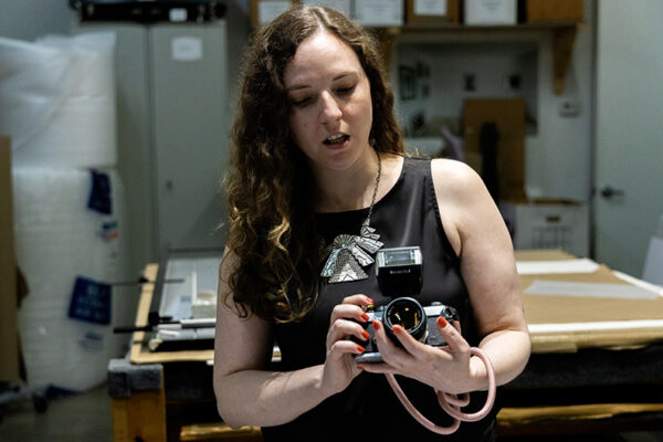 A woman in a sleevless black t-shirt demonstrates how to use a camera.