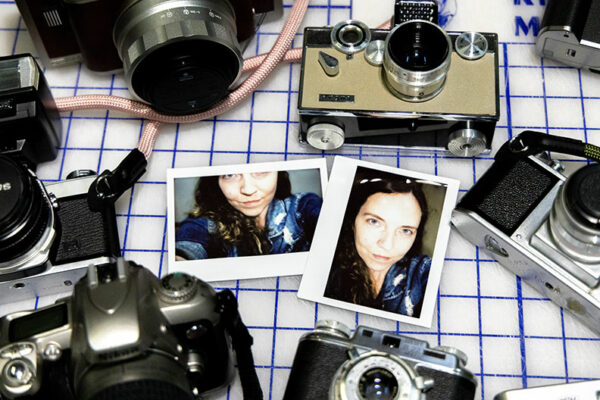 A table top full of different styles of cameras and two polaroid photographs of a woman's face.