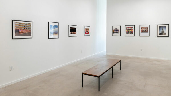 Several framed photographs hang on a gallery wall before a bench.