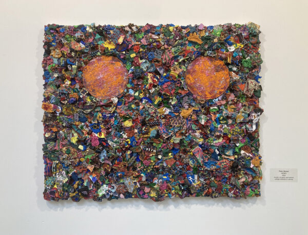 A rectangular panel consisting of many small fragments of plastic and detritus, with two orange orbs near the top edge of the piece.