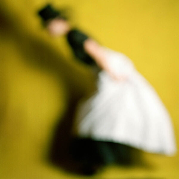 A blurred photograph of a figure wearing a top hat and set against a yellow background.