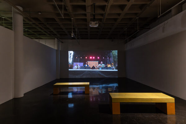 A darkened gallery hosts a projection of a musical performance.