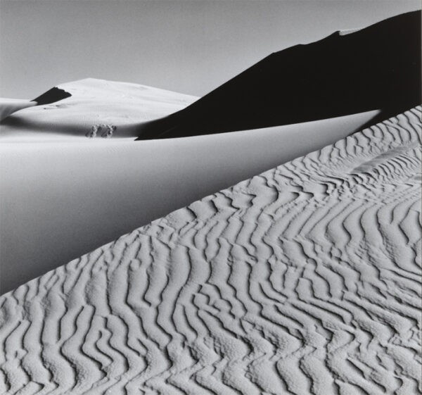 A black and white photograph of rippled sand dunes.