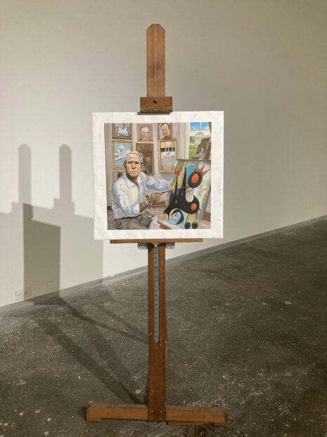 A painting of George W. Bush in a home studio, surrounded by small paintings of Dallas and SMU architecture.