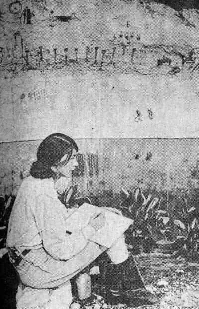 A black and white photograph of a seated woman painting watercolors in a sketchbook.