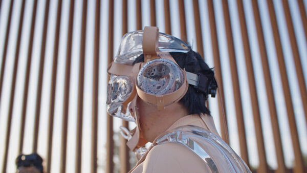 A person walks wearing a mask and goggles past the U.S. border wall.