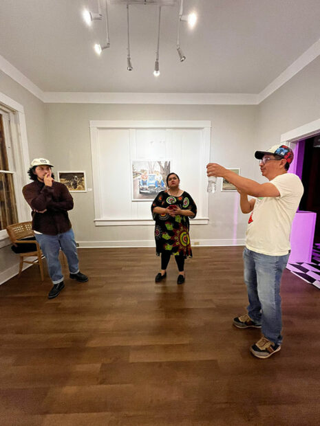 Three people stand in the center of a gallery with paintings on its walls.