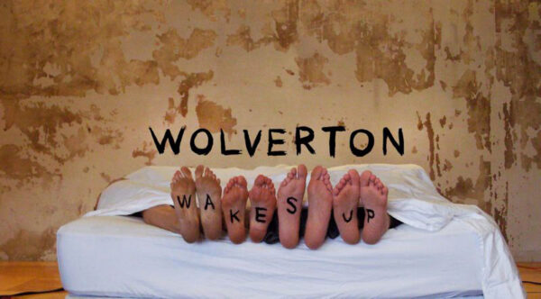 A poster advertising a band which reads "Wolverton wakes up," with the phrase "wakes up" written on the bottom of the bandmembers' feet.