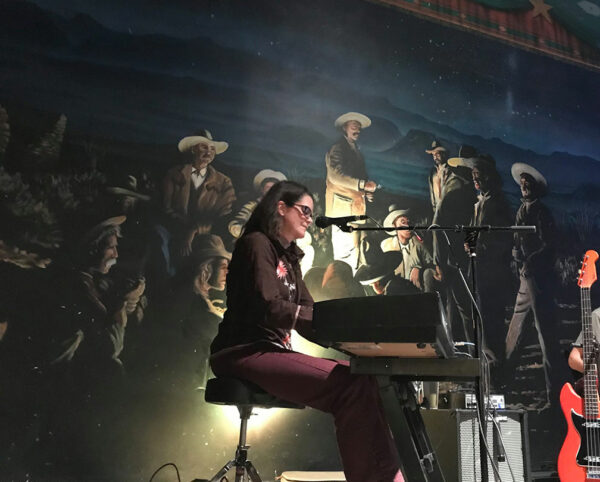 A woman plays keyboards at a theater with painted backdrop.