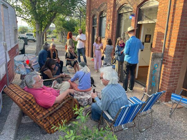 A group of people lounge around outside of a gallery on an opening night.