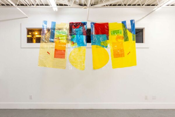 A colorfully painted tapestry on vinyl hangs in front of a window in a gallery.