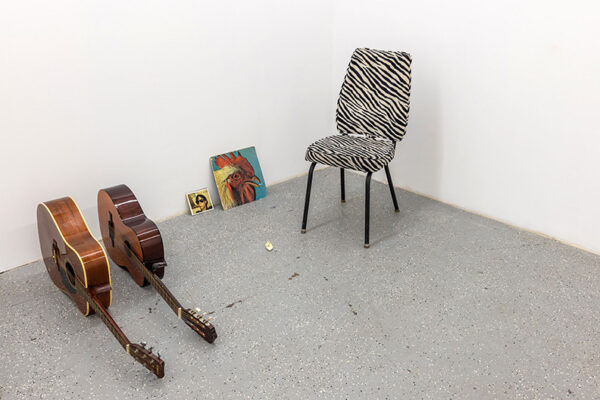 Two guitars an LP and a CD sit on the floor of a gallery next to a zebra-striped chair.