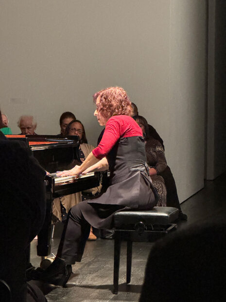 A woman performs at a grand piano in a gallery in front of an audience.