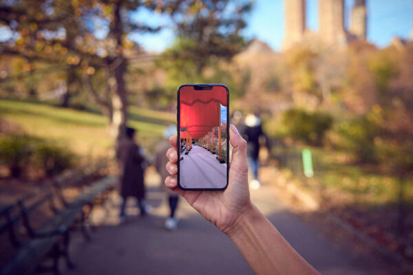 A hand holds a cell phone that displays an AR image of Christo's "The Gates" in Central Park.