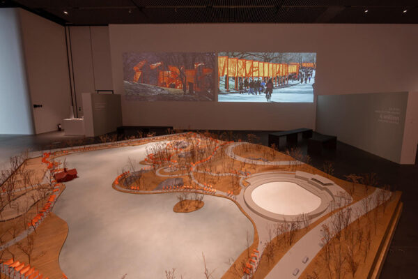 A model of Central Park is installed in front of a video projection in a gallery.