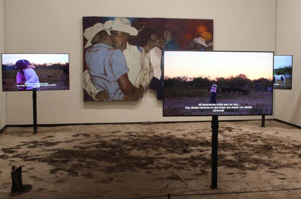 Several video screens installed in a gallery with dirt on the floor.