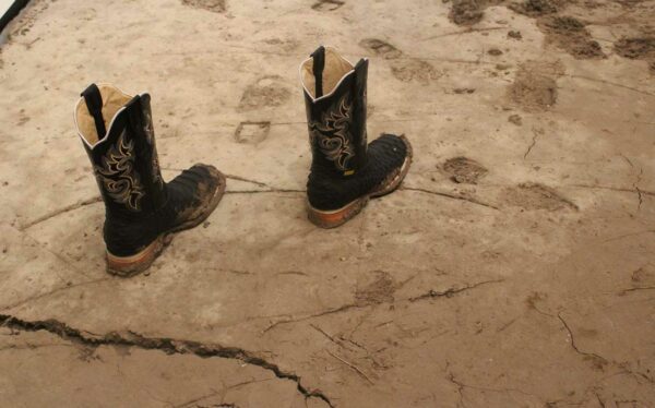 Two cowboy boots stand upright on a dirt floor.