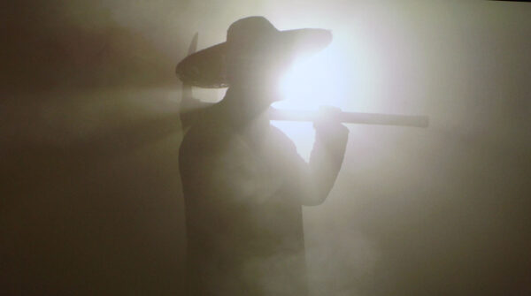 A person in a cowboy holding a pickaxe is silhouetted.. 