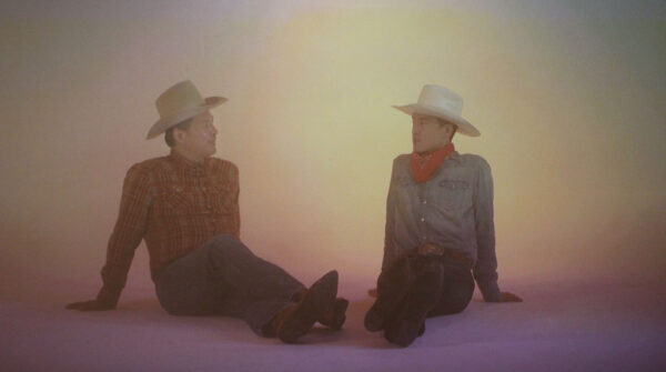 Two cowboys sit together and talk.