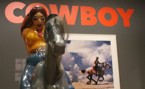 A fiberglass sculpture of a woman on a horse with a framed photogrpah of a cowboy on a horse in the background.