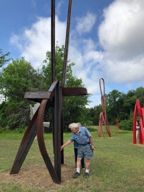 A photograph of Mac Whitney walking around his large sculptures in a green field.