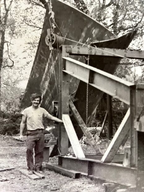 A black and white photograph of a Mac Whitney standing next to a large sculpture.