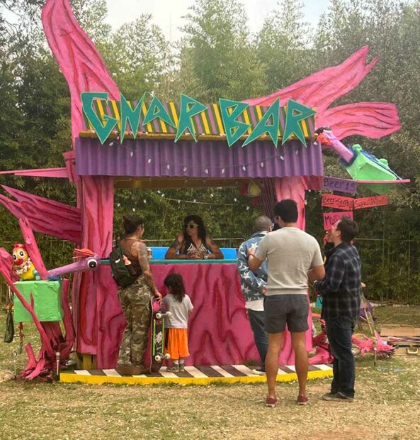 A pink and purple covered bar with sculptures attached to it and customers waiting in line.