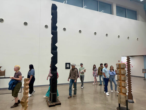 People walk through a large gallery filled with wooden sculptures.