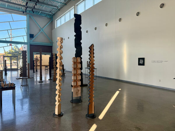 Tall, totemic wooden sculptures stand in clusters in a large gallery