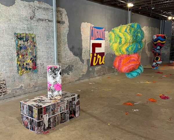 A gallery with raw and unfinished walls hosts sculptures and paintings.