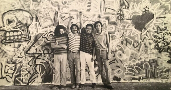 Four men stand together in fron of a large mural.