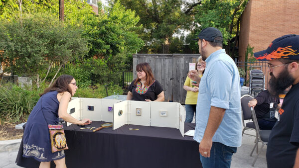 A photograph of Mary Cantú and others displaying a small gallery of works made out of white binders.