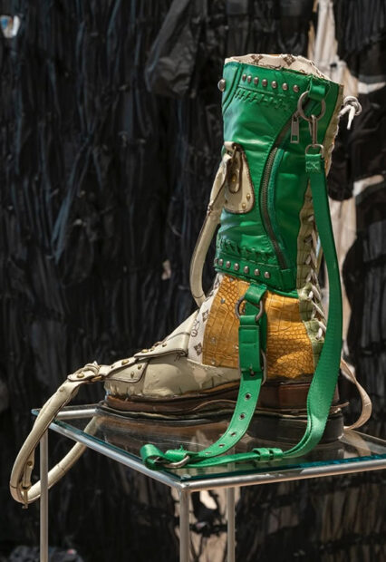 A boot, made from scraps of other garments sits atop a pedestal in a gallery.