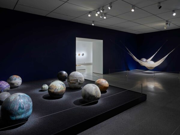 Installation photograph of a ceramics exhibition, featuring multiple works hug on and displayed against walls and plinths.