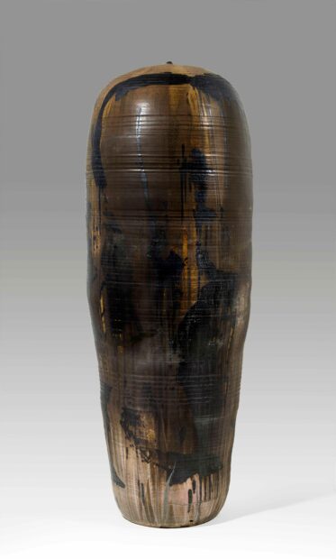 A long, tall ceramic glazed in abstract gestures on a brown ground.