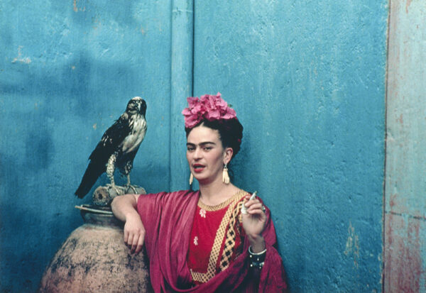 A photograph by Nickolas Muray featuring the artist Friday Kahlo with her pet eagle, standing against a blue wall.