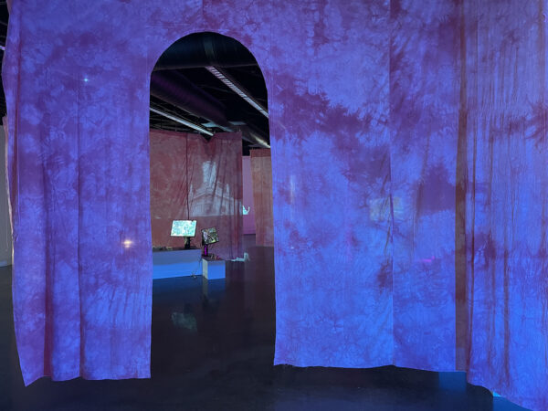 An installation image depicting tv monitors and video projects with hanging curtains dividing the space. 