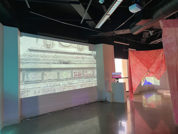 An installation image depicting tv monitors and video projects with hanging curtains dividing the space. 
