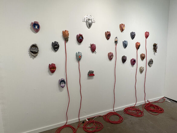 Celia-Eberle-at-Cris-Worley-Fine-Art_Dallas-Art-Fair-1 24 sculpted hearts hang on the wall of an art fair booth.