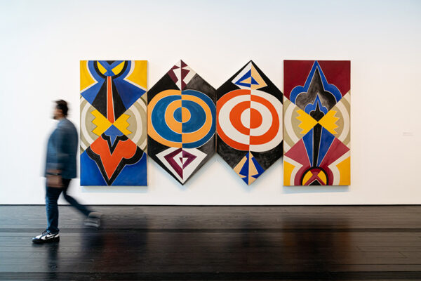 A man walks past four large abstract canvases.