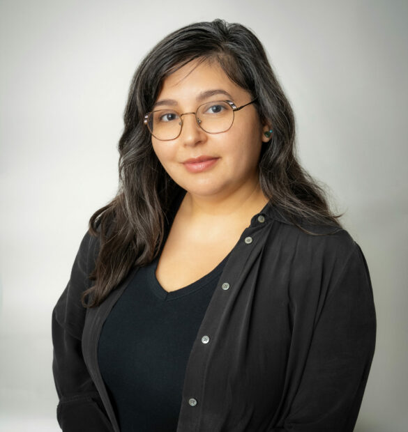 A photograph headshot of a Latinx woman. She is wearing a black cardigan and shirt and glasses.
