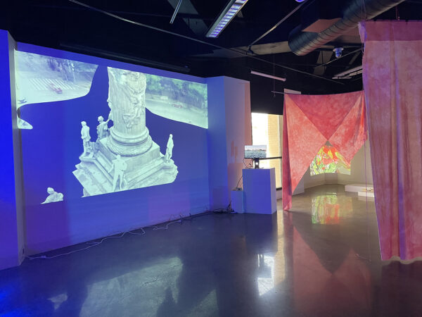 An installation image depicting tv monitors and video projects with hanging curtains dividing the space. 