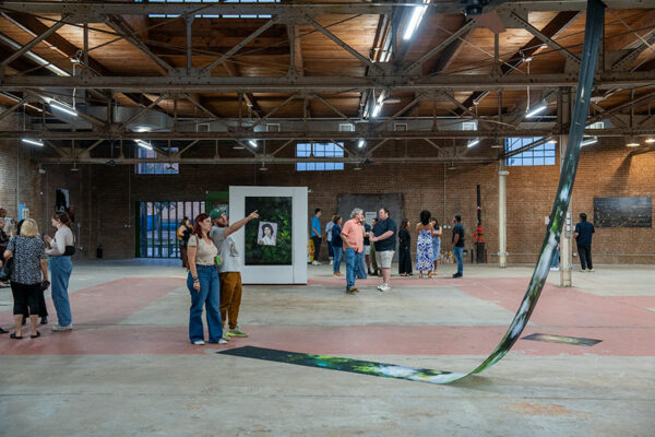 Several people walk through a large brick walled gallery looking at photo-based artworks.
