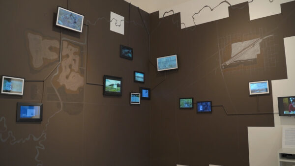 An installation image featuring small screens hung on a gray and white painted wall.