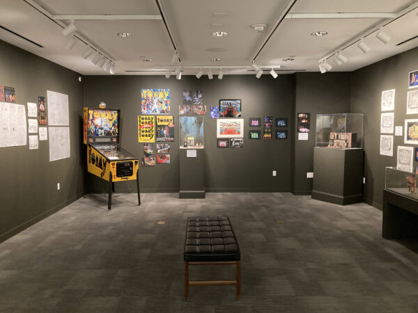 An interior gallery space is hung with illustrations, photographs, and one pinball machine.