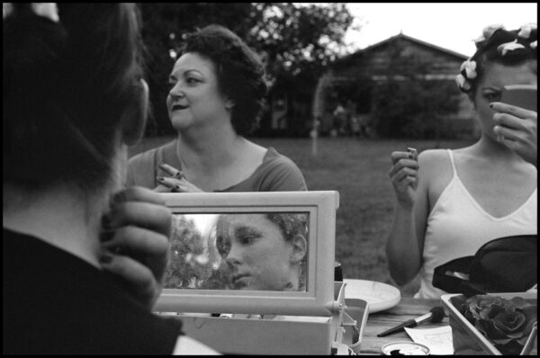 A black and white photograph of actors putting on makeup before a performance.